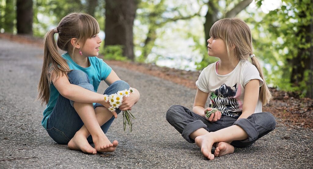 two children sitting down, looking at each other while having a meaningful conversation